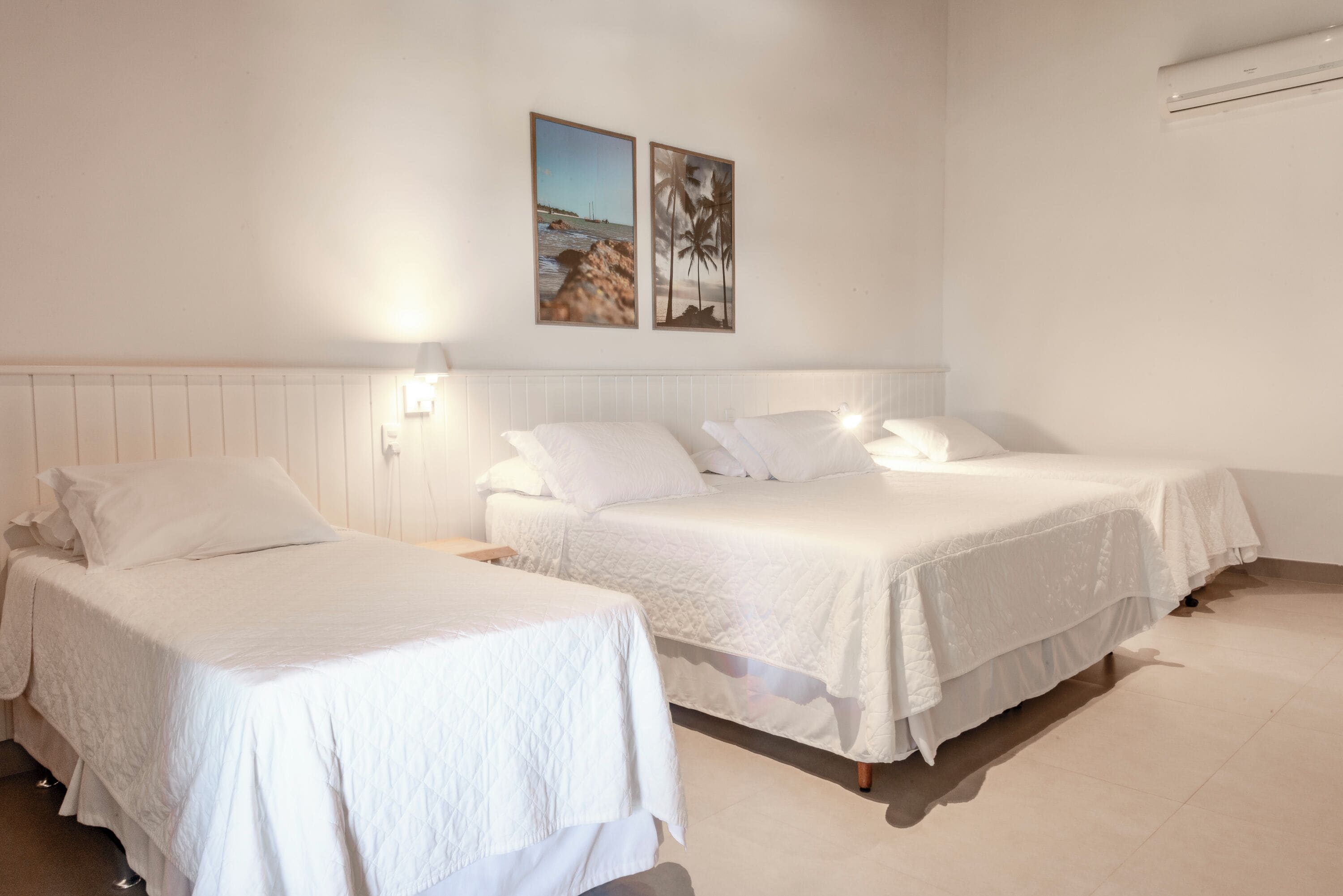 A hotel room with two beds, white bedding, a nightstand, and wall-mounted artwork.