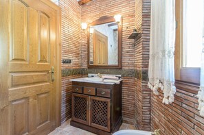 A bathroom with a wooden door, a sink with a mirror above it, and a window with a curtain.