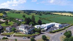 A large building with a parking lot, surrounded by green fields and a few houses.