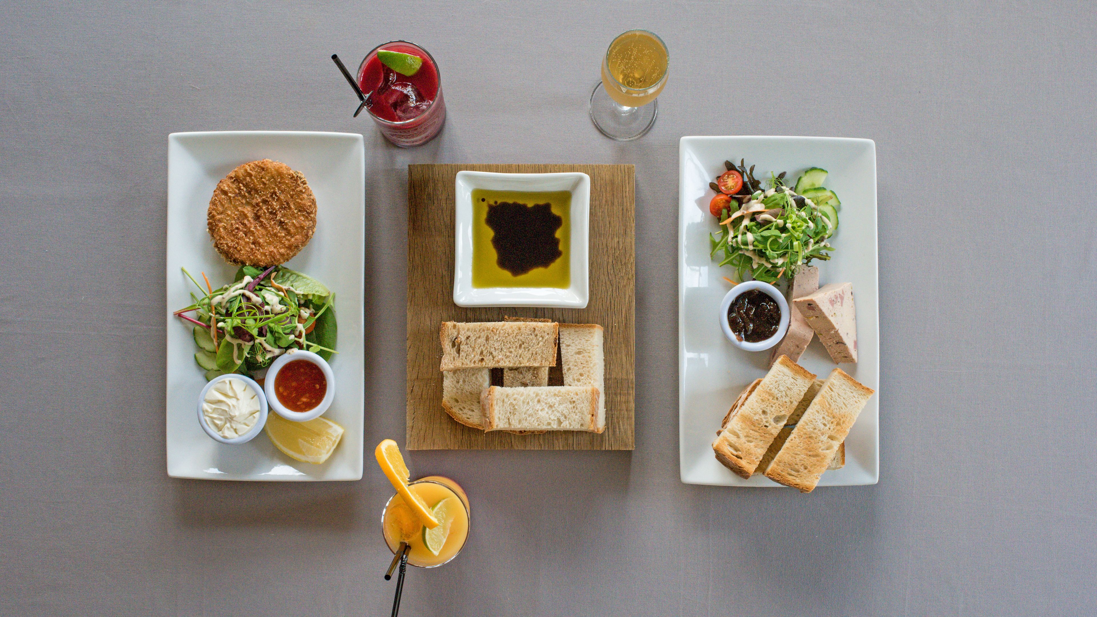 Una mesa con diversos alimentos, incluyendo pan, ensalada y una bebida.