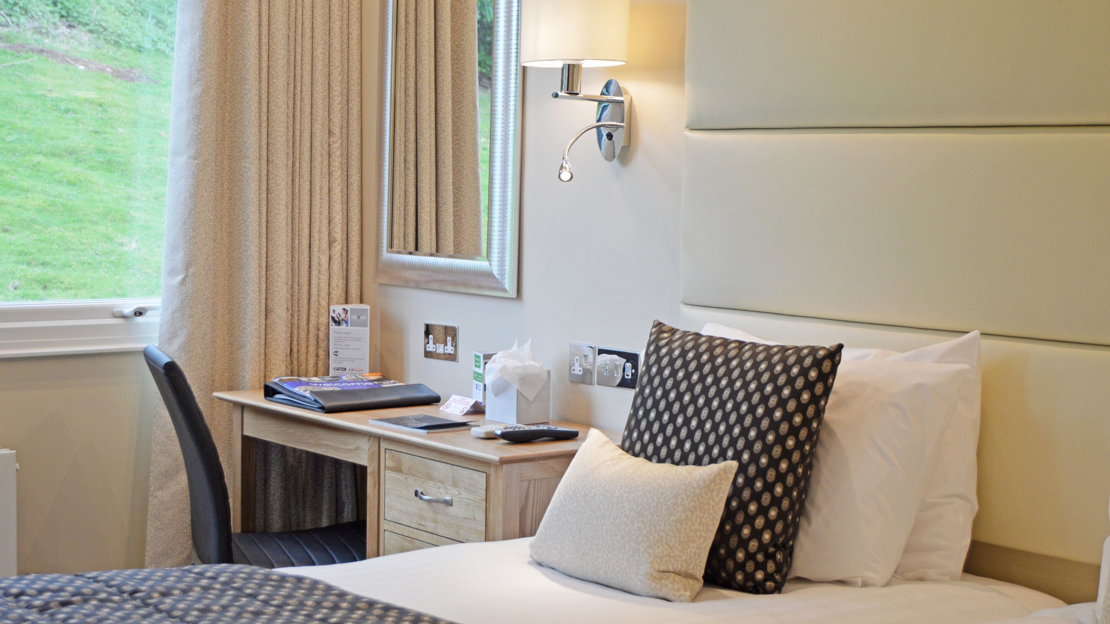 A hotel room with a bed, a desk with a computer, a lamp, and a window with curtains.