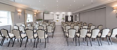 A conference room with rows of chairs facing a presentation screen, a small table with a plant, and a door labeled "Private."