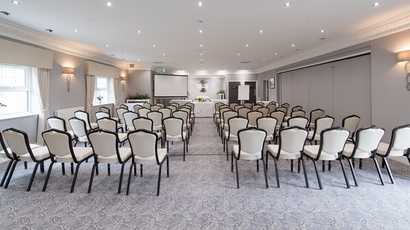 A conference room with rows of chairs facing a presentation screen, a small table with a plant, and a door labeled "Private."