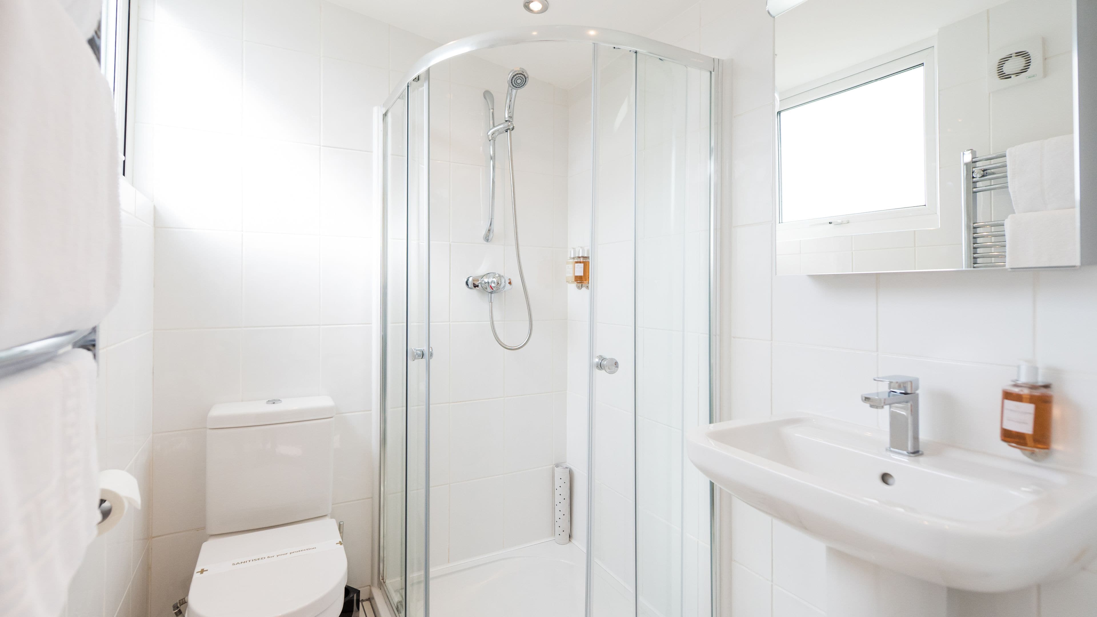 A modern bathroom with a glass-enclosed shower, a white toilet, and a sink with a mirror above it.