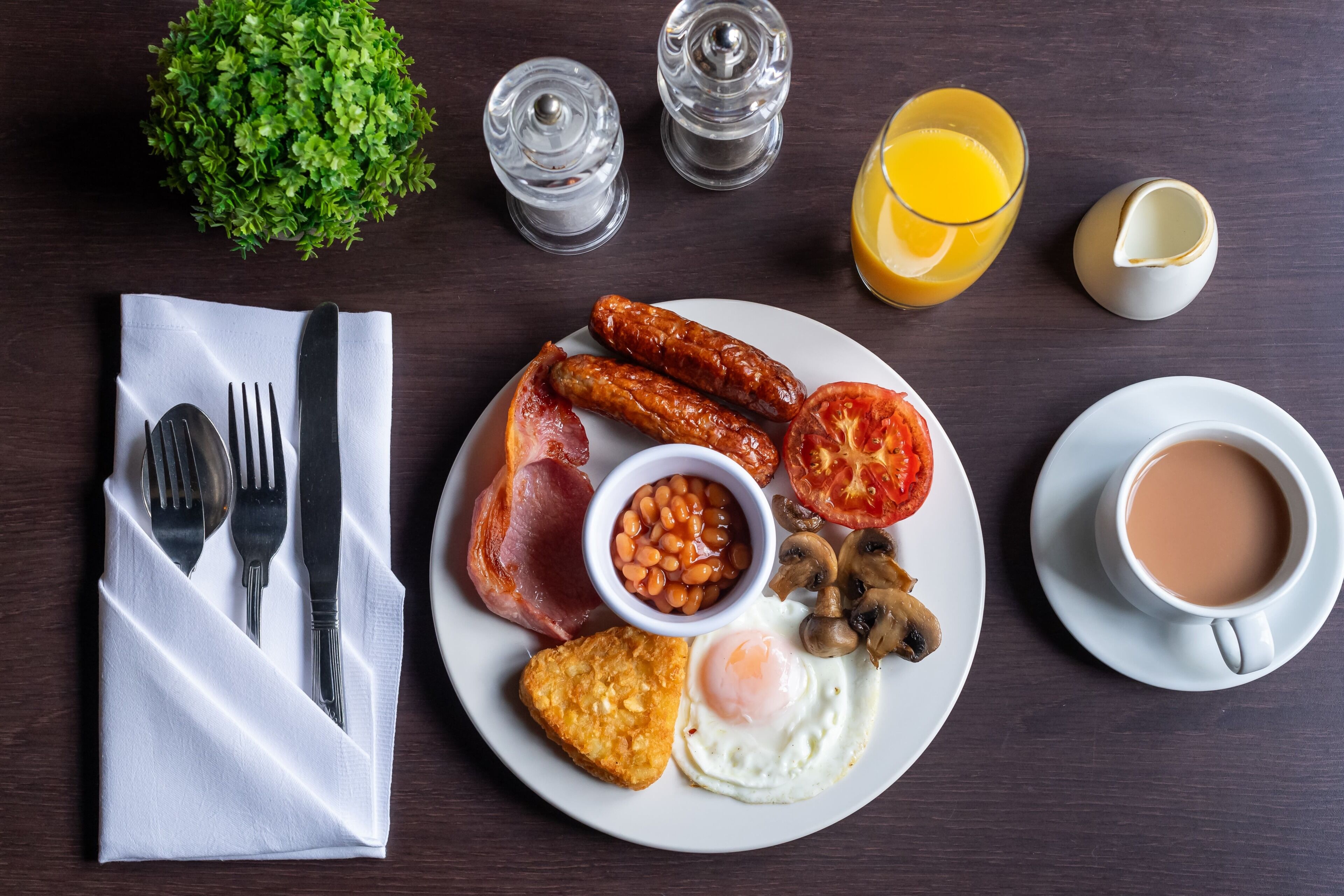 A breakfast plate with sausages, bacon, eggs, mushrooms, baked beans, and a tomato.