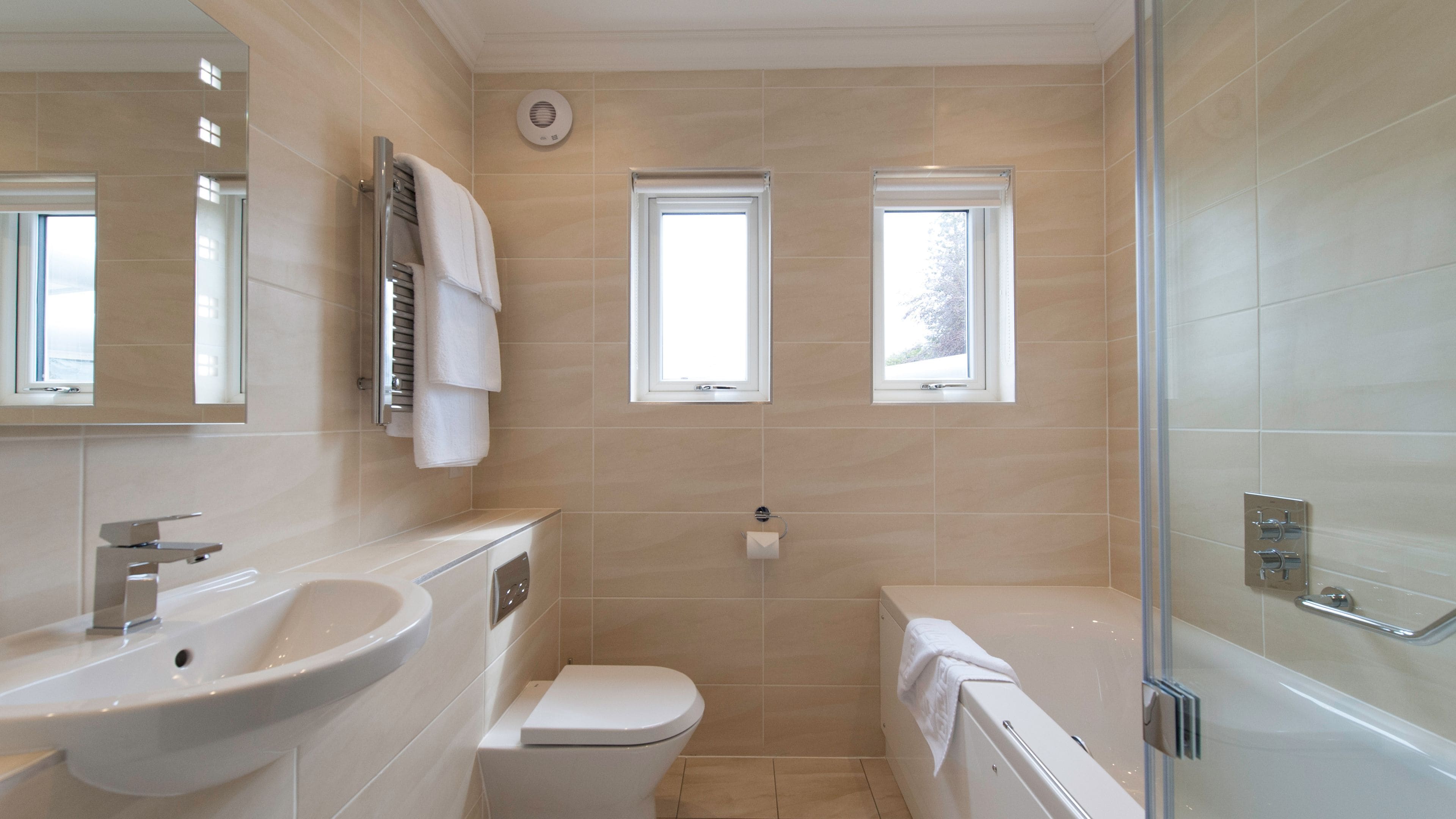 A modern bathroom with a sink, toilet, bathtub, and two windows.