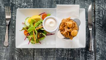 A white rectangular plate with a salad, a bowl of dipping sauce, and a basket of fried food on a wooden table.