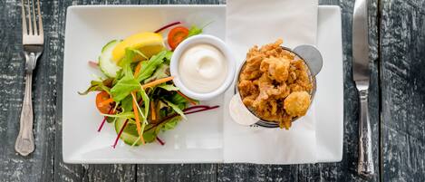 A white rectangular plate with a salad, a bowl of dipping sauce, and a basket of fried food on a wooden table.