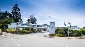 A modern hotel with a curved facade, a prominent sign, and a well-maintained garden.