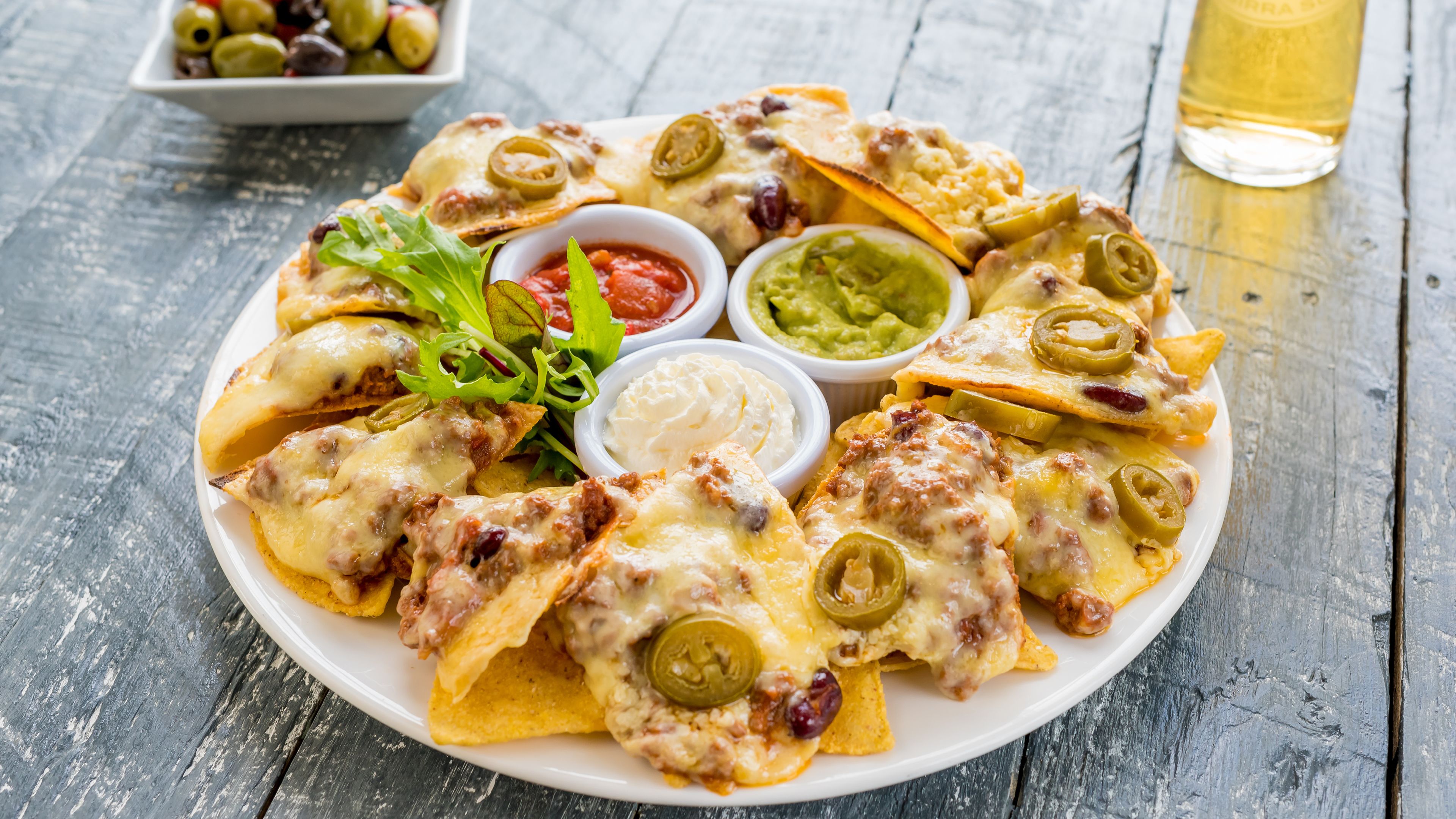 A plate of nachos with cheese, jalapeños, and a side of guacamole and sour cream.
