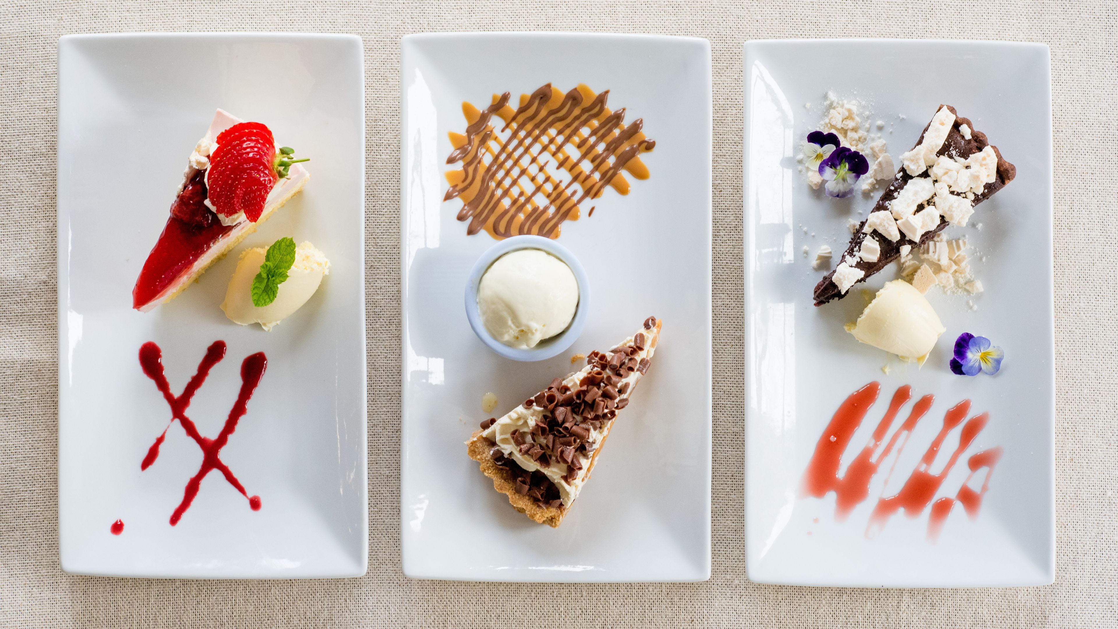 Three square white plates with desserts and sauces.