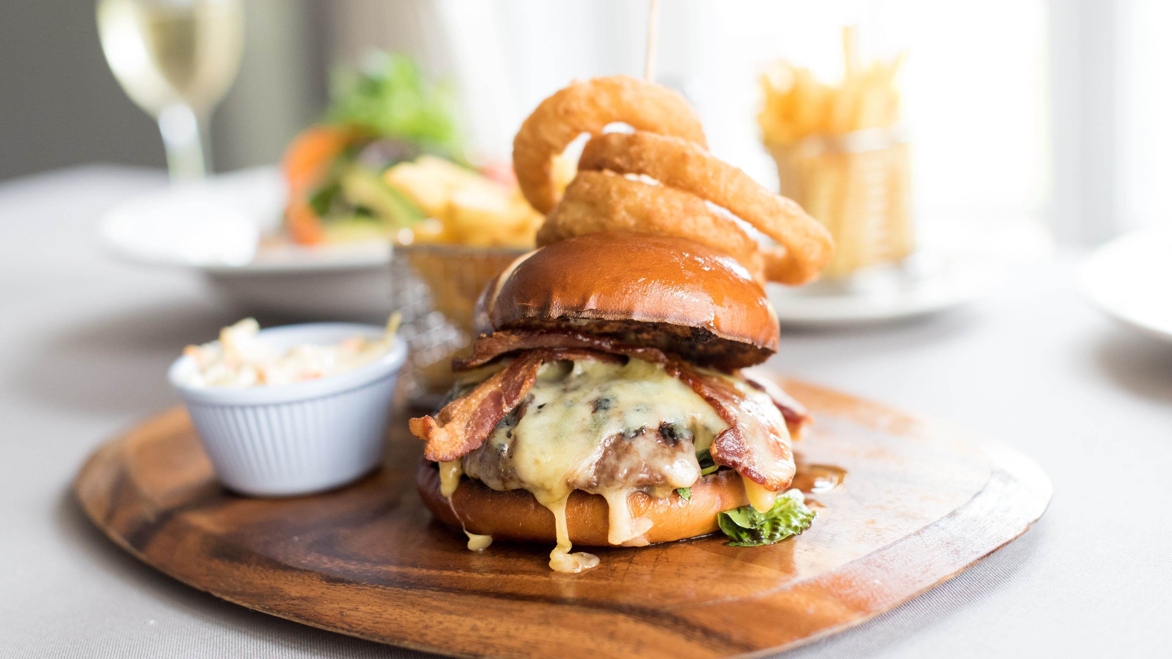 A burger with cheese and bacon on a bun, served with fries and a small bowl of coleslaw.