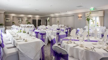 A banquet hall with round tables set for a formal event, featuring white tablecloths and purple sashes.