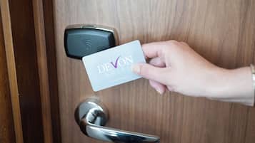 Una mano sostiene una tarjeta con la inscripción 'DEVON HOTEL', acercándose a una puerta con cerradura digital.