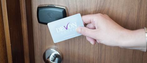 A hand holding a card with 'DEVON HOTEL' written on it, approaching a door with a digital lock.