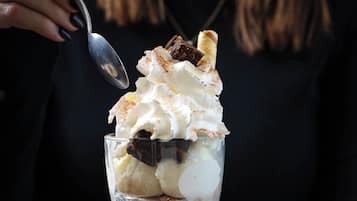 A dessert in a clear glass cup with whipped cream and chocolate pieces.