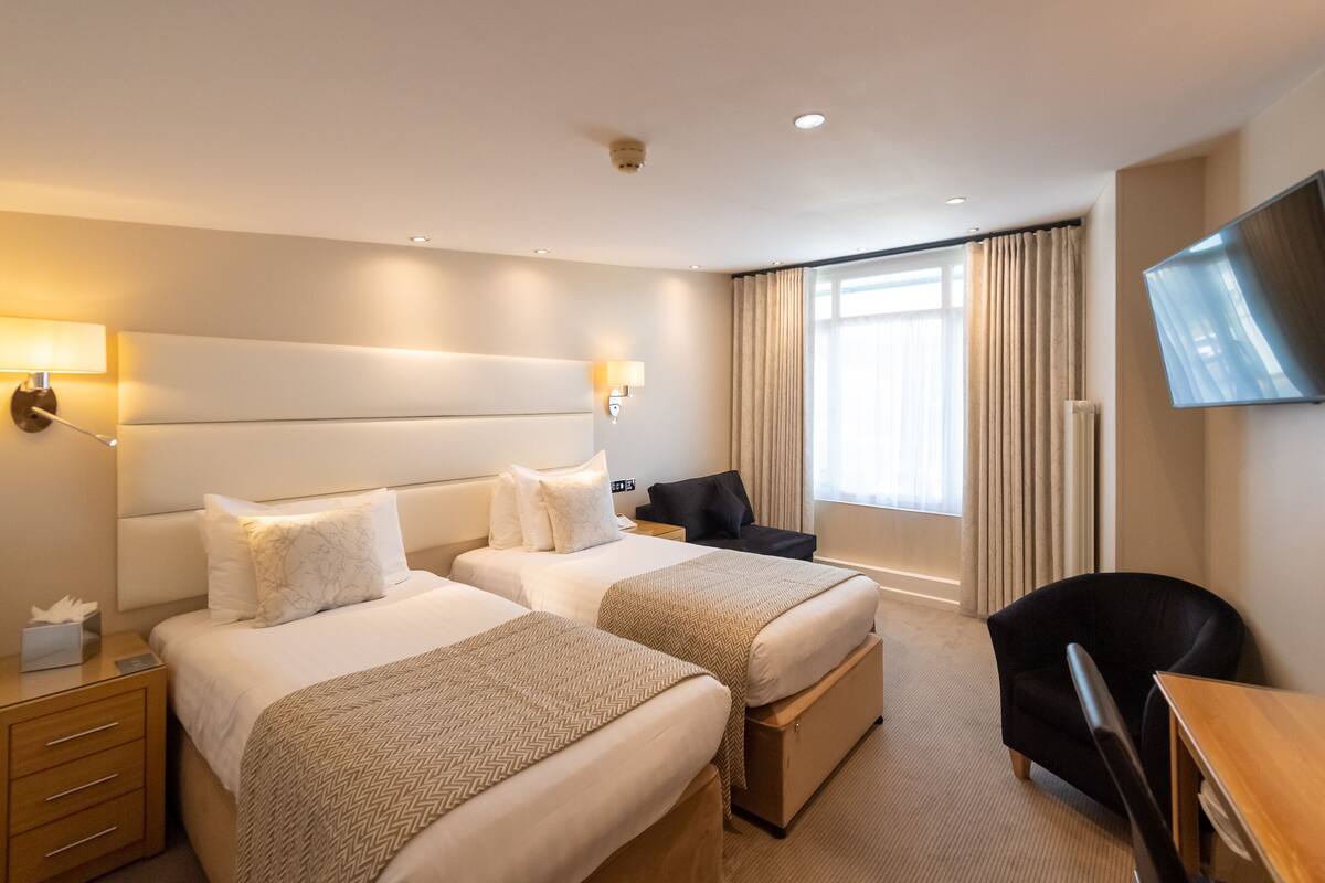 Habitación de hotel con dos camas, un escritorio, una silla, un televisor y una ventana con cortinas.