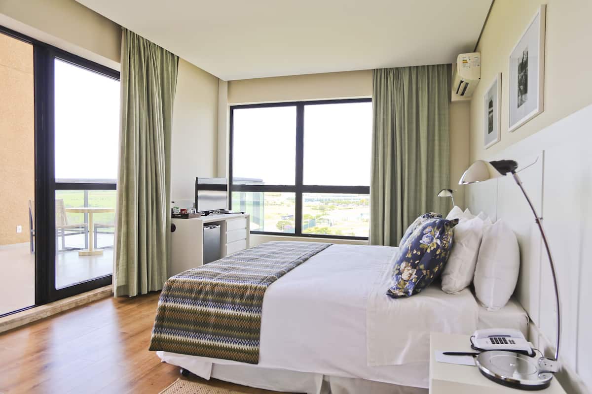 Een hotelkamer met een groot bed, een bureau met lamp, een telefoon en een raam met gordijnen.