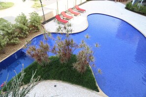 Une piscine entourée de verdure, avec des chaises longues rouges.