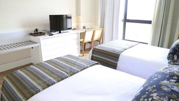 Habitació d'hotel amb dos llits, un escriptori, una televisió i una finestra amb cortines.
