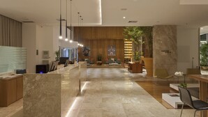 A modern reception area with a marble reception desk, seating area, and a large plant. - Vitória Hotel Convention Paulínia (Paulinia)