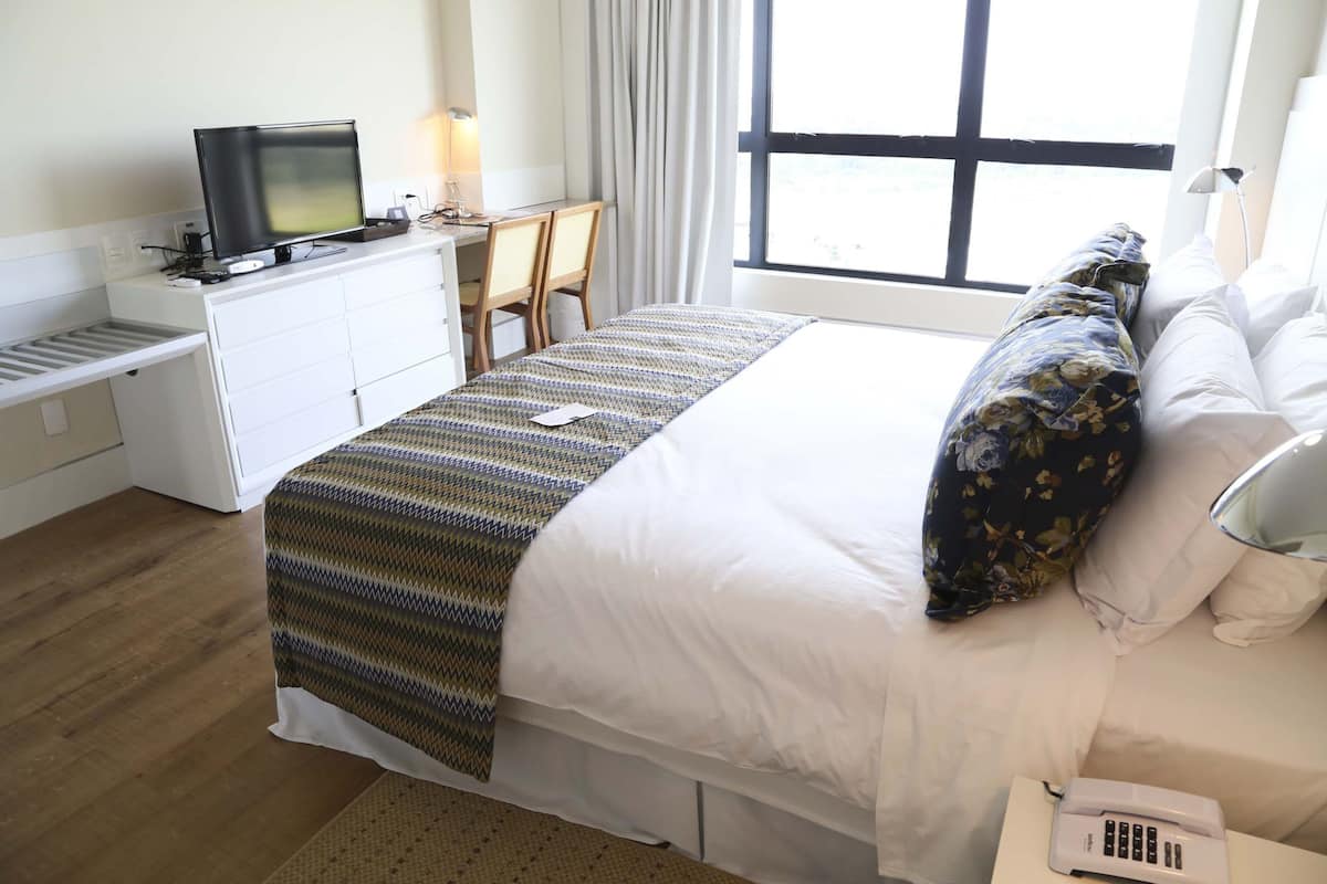 Hotelkamer met een bed, een bureau met een computer en een televisie, een telefoon en een raam met gordijnen.
