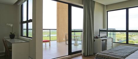 Een moderne hotelkamer met balkon, bureau, bed en uitzicht over de stad.