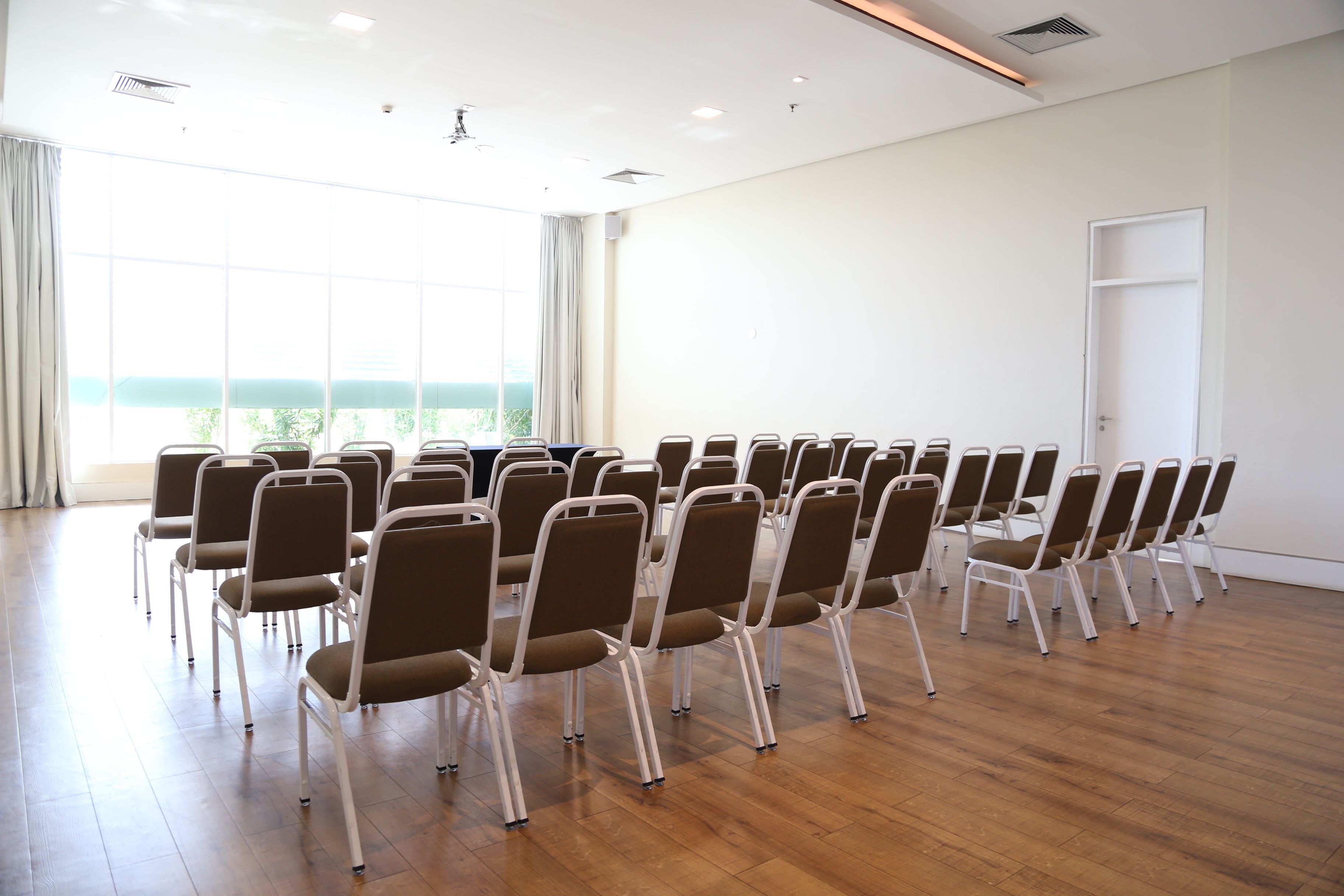 Un salón de conferencias con filas de sillas, ventanas amplias y una puerta.