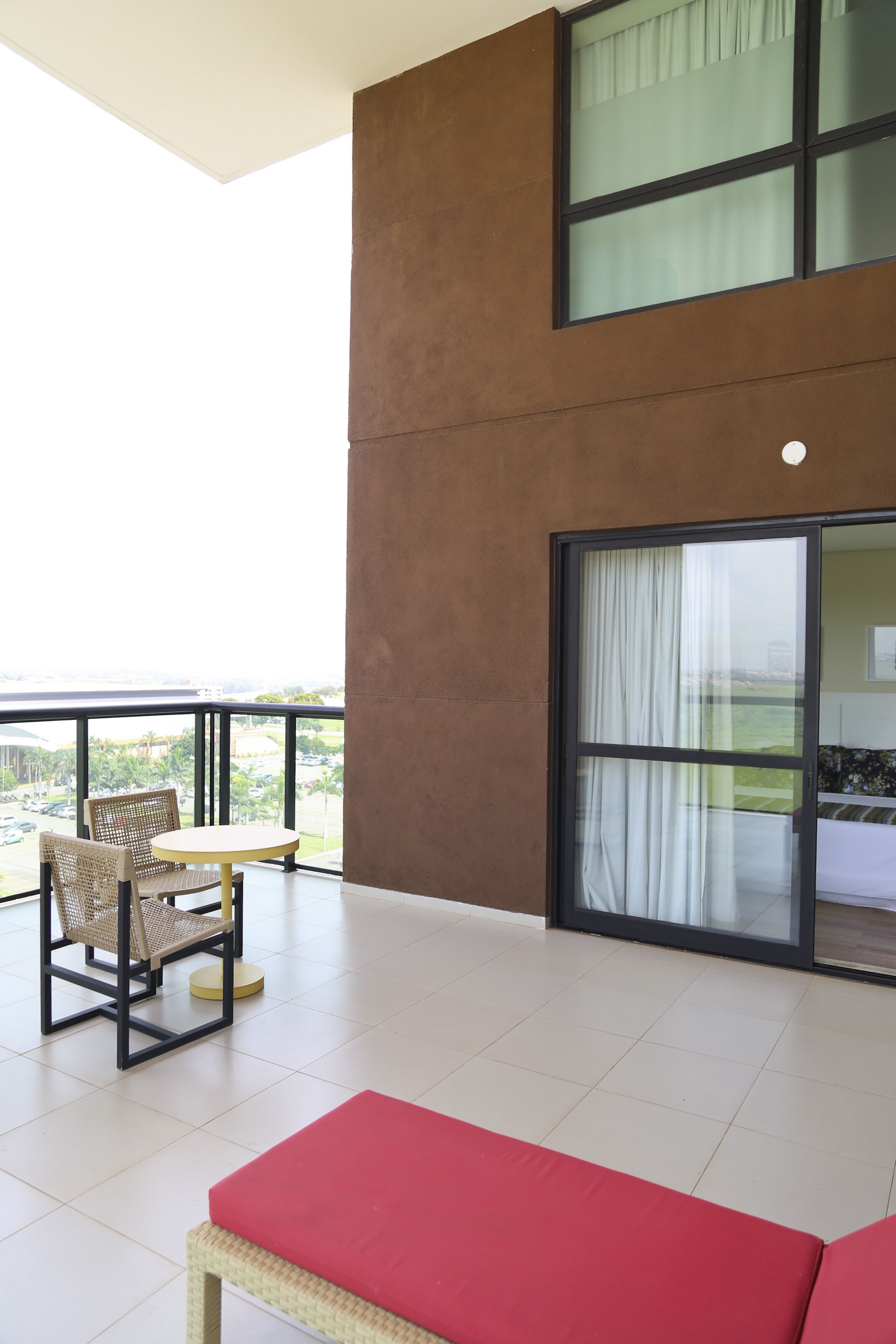 Uma varanda com mobiliário de vime, um banco vermelho e vista para a cidade.