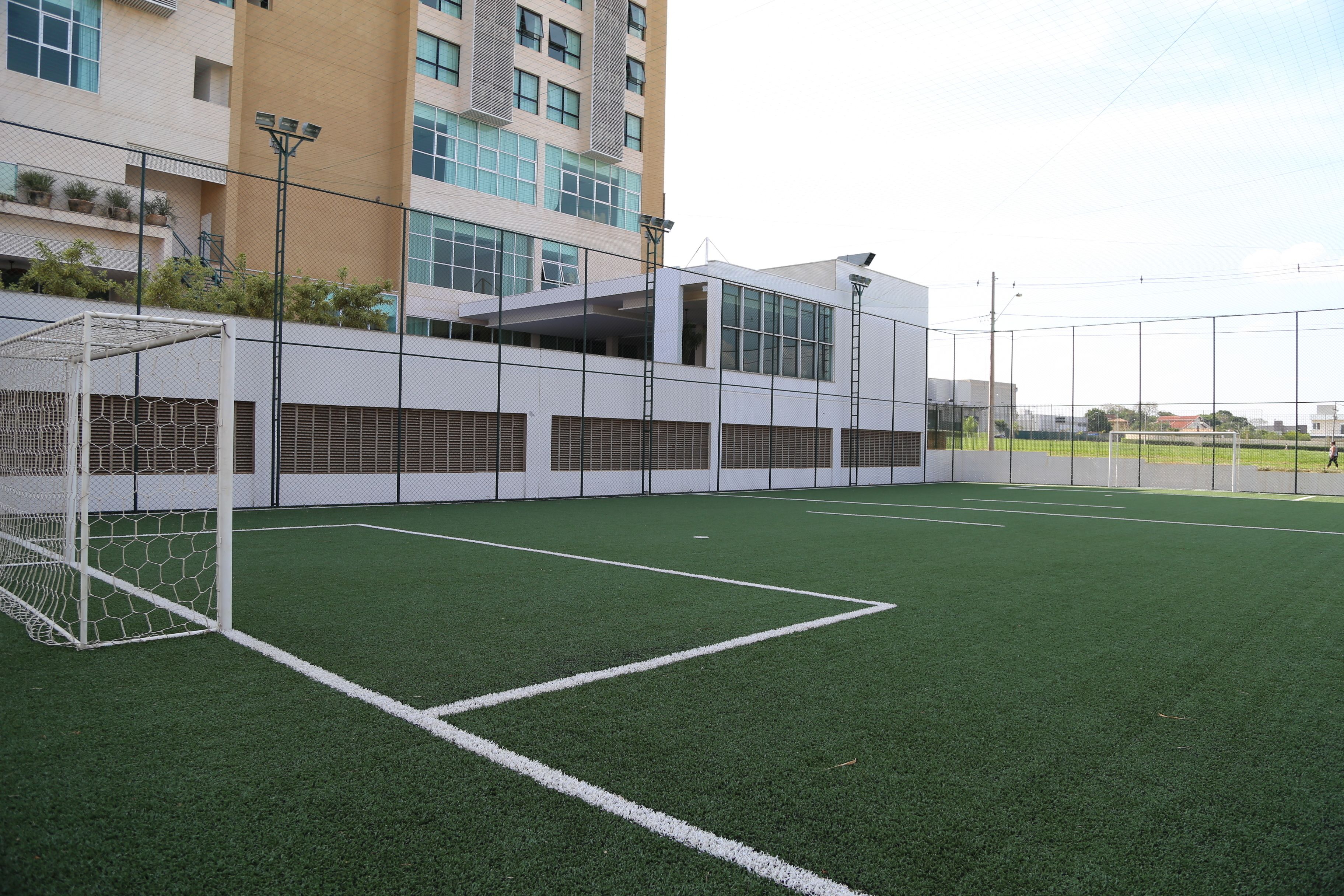 An indoor soccer field with a goal, surrounded by a fence and a building with multiple windows and balconies.