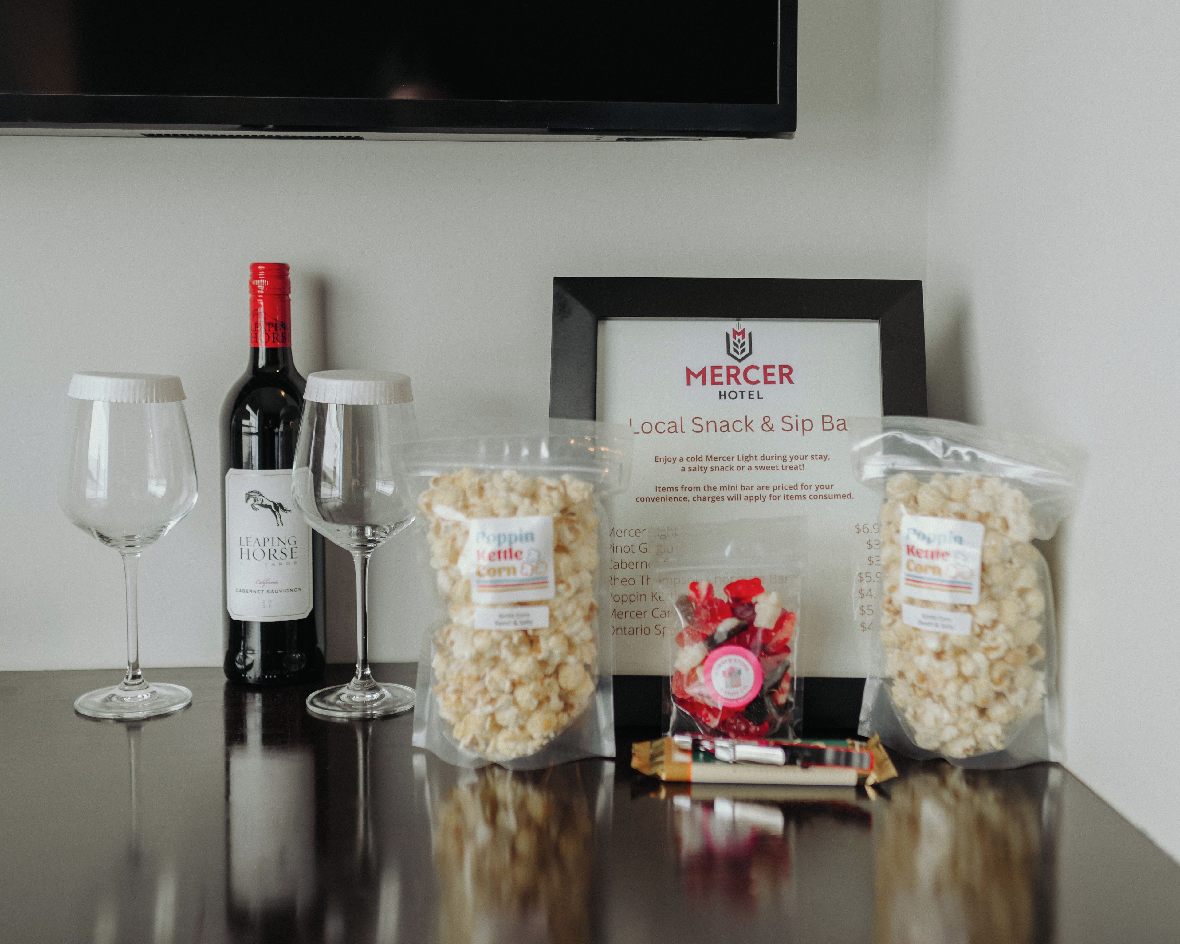 A table with a wine bottle, two wine glasses, popcorn, and a snack bar sign.