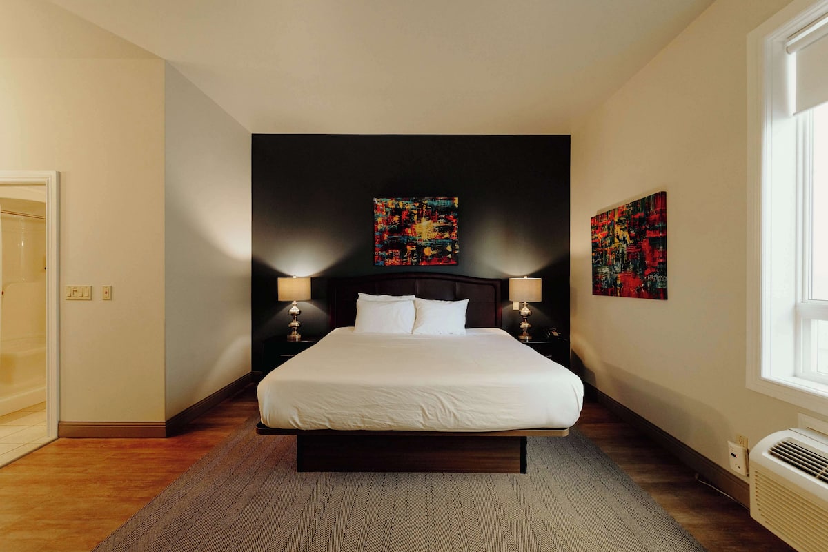 A modern hotel room with a large bed, two bedside lamps, and abstract art on the walls.