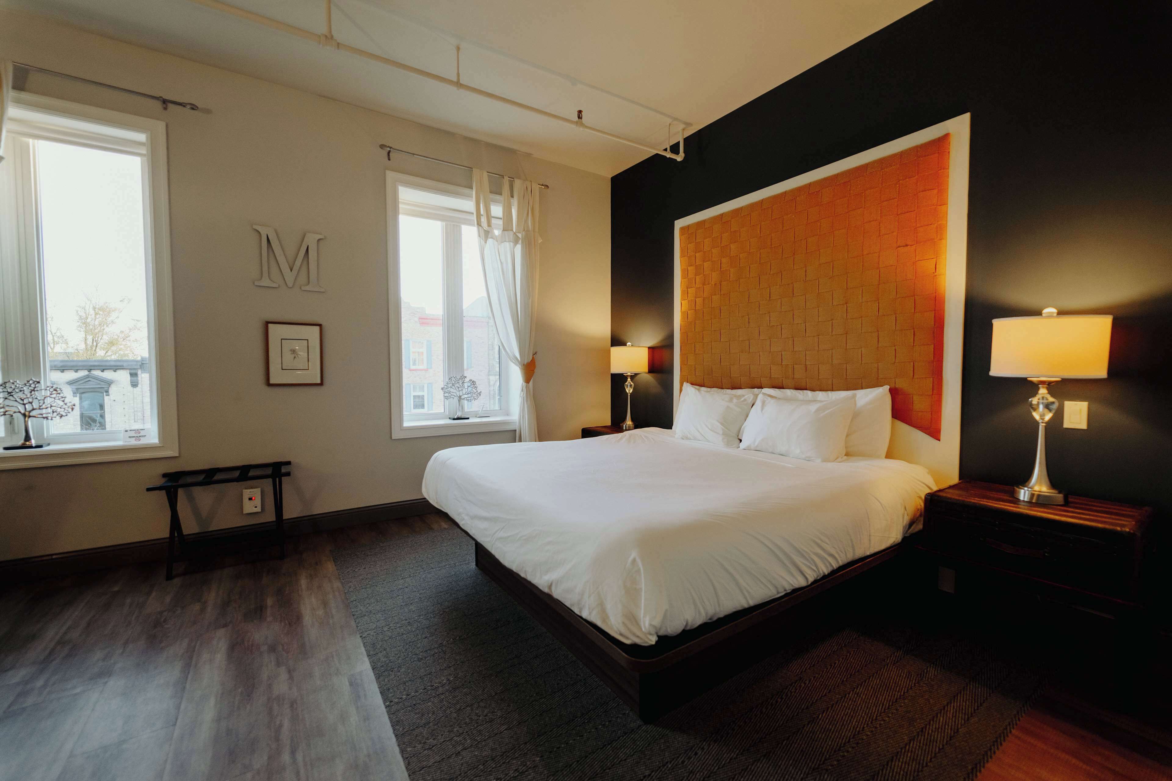 Habitación de hotel con una cama grande, dos mesitas de noche con lámparas, una ventana con cortinas y un cabecero fijado a la pared.