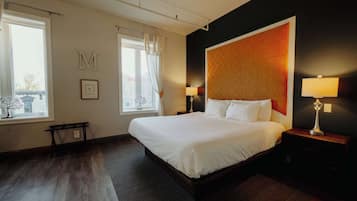 Habitación de hotel con una cama grande, dos mesitas de noche con lámparas, una ventana con cortinas y un cabecero fijado a la pared.