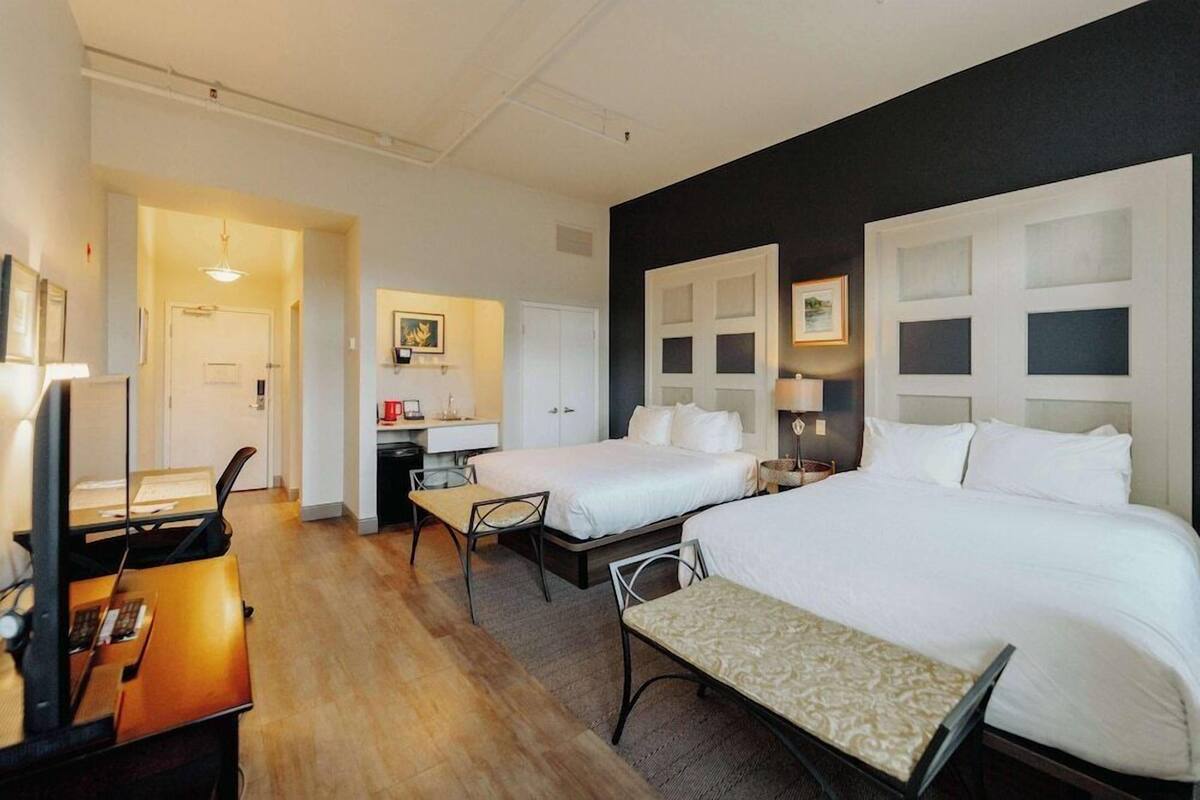 A hotel room with two beds, a desk, a chair, and a small table.
