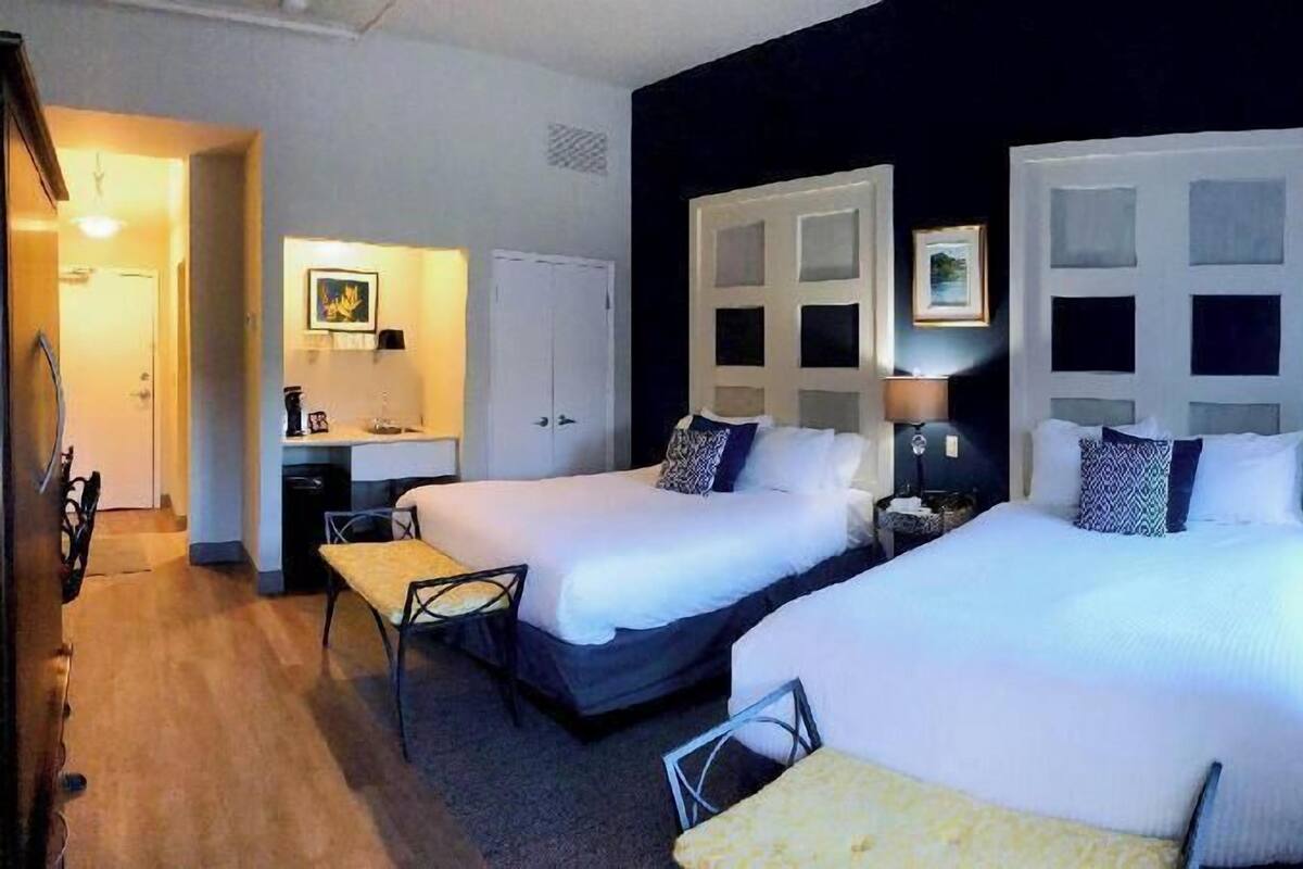 A hotel room with two beds, a desk, a chair, and a wardrobe.