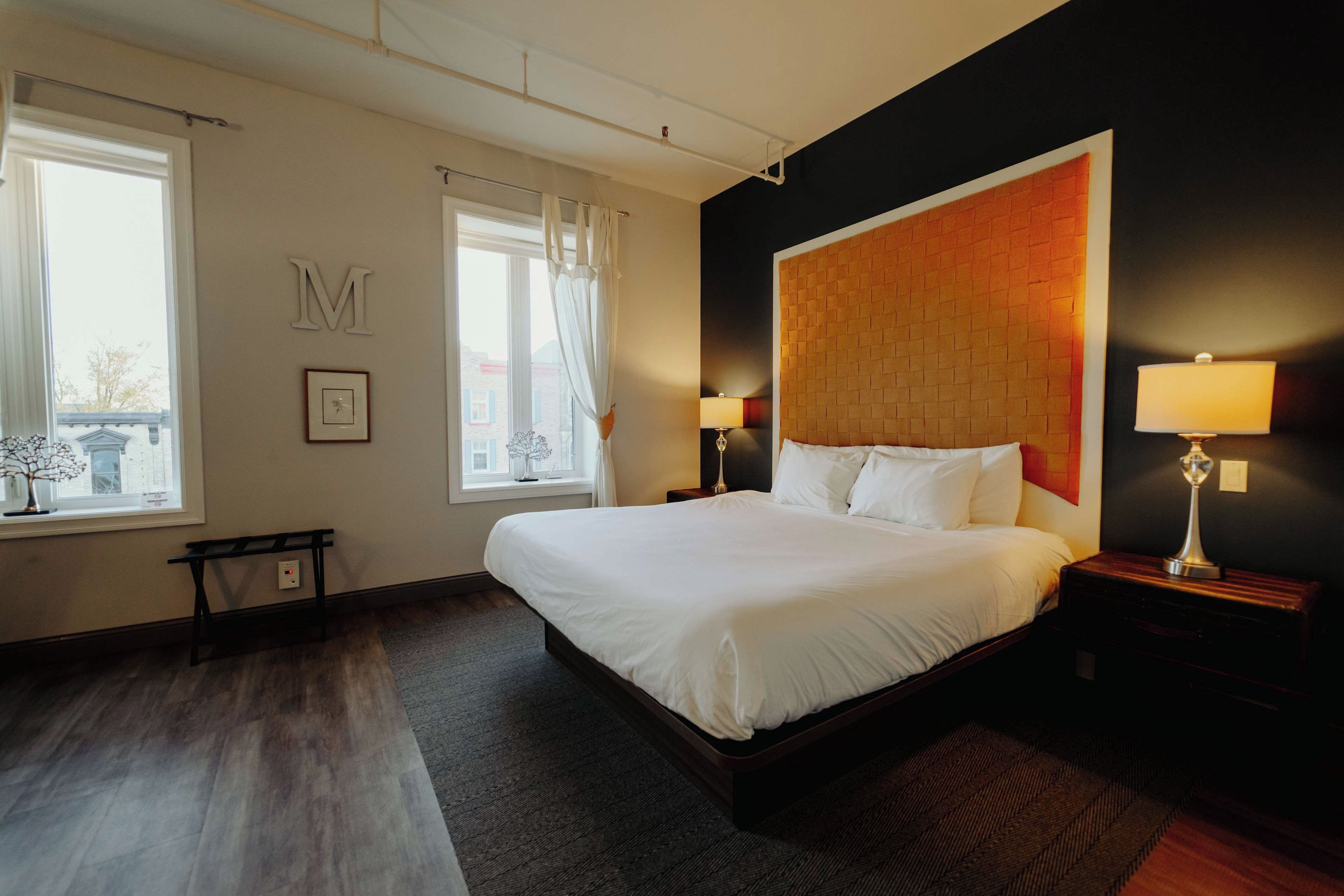 Ein Hotelzimmer mit einem großen Bett, zwei Nachttischen mit Lampen, einem fenster mit Vorhängen und einem am Wand montierten Kopfteil.