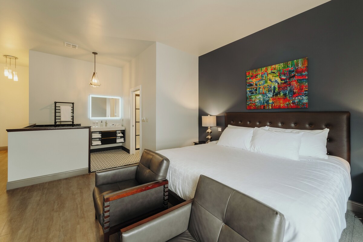Een hotelkamer met een groot bed, een bureau, een stoel, een spiegel, een schilderij en een lamp.
