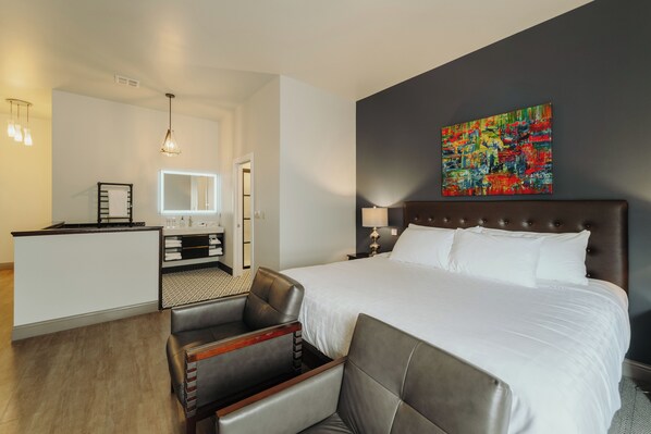 A hotel room with a large bed, a desk, a chair, a mirror, a painting, and a lamp.