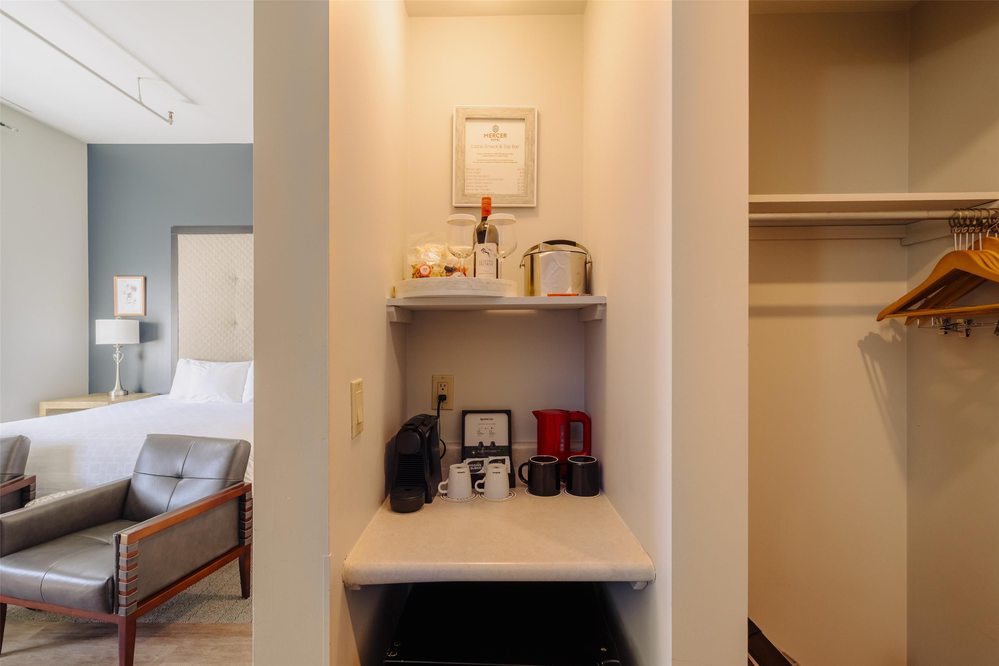 A hotel room with a bed, a chair, a minibar, a coffee maker, and a framed sign on the wall.