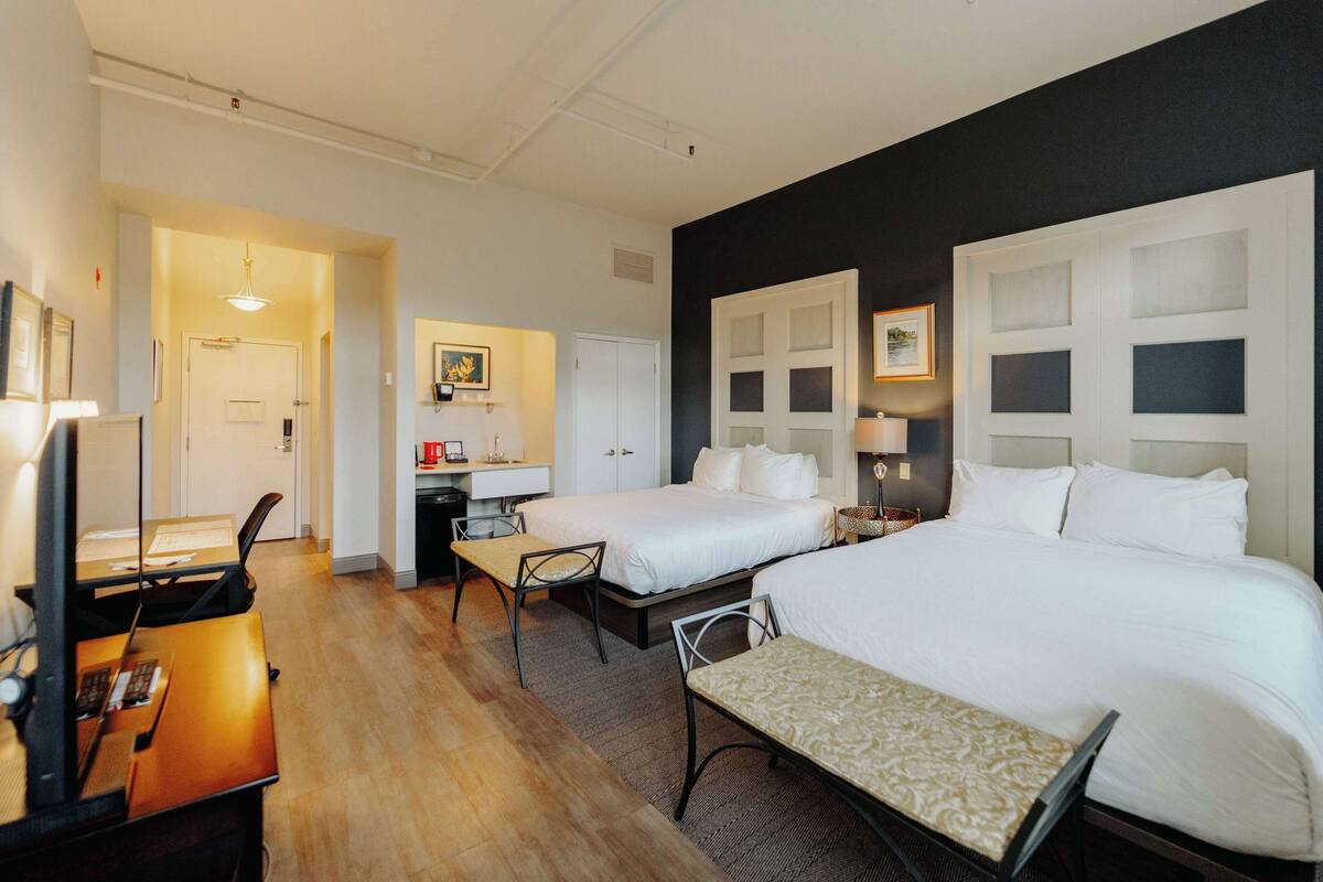 A hotel room with two beds, a desk, a chair, and a small table.