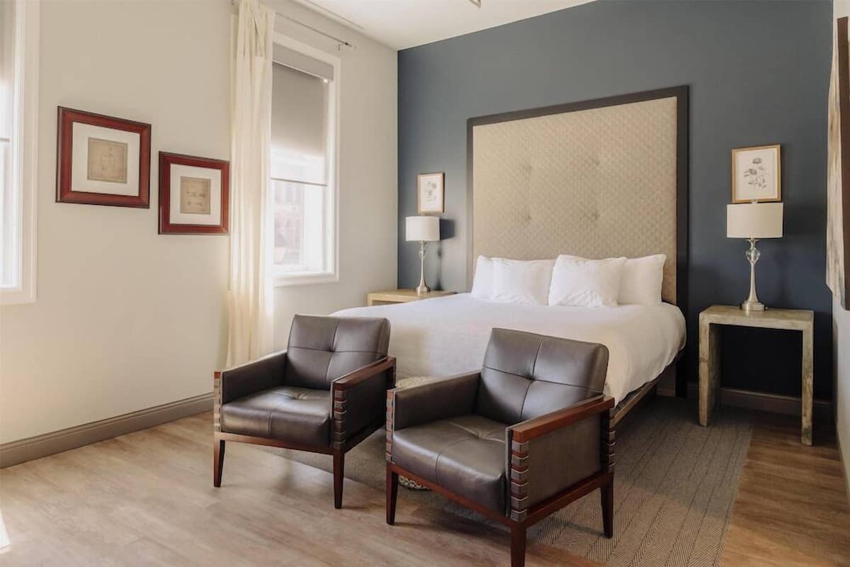 A bedroom with a large bed, two nightstands, two chairs, and framed pictures on the wall.