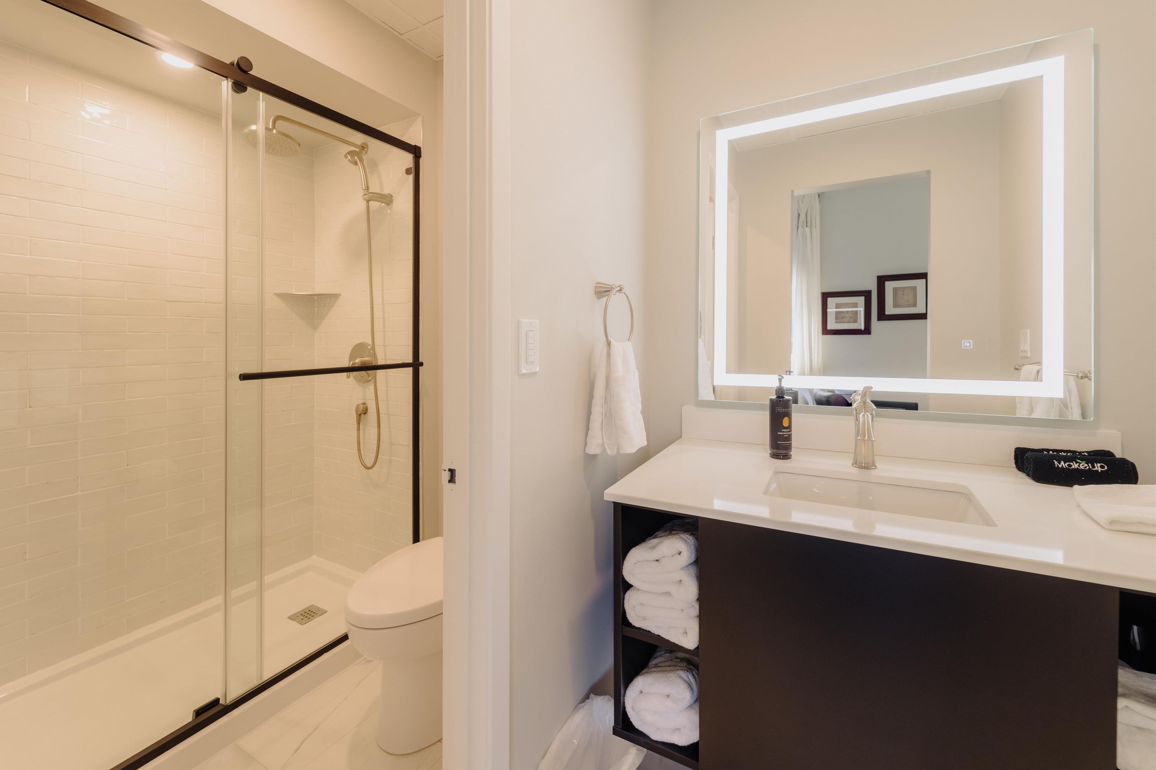 Un baño moderno con ducha de vidrio, lavamanos blanco y un espejo grande.