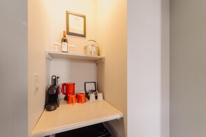 Een kitchenette met een koffiezetapparaat, mokken, een fles wijn en een ingelijst certificaat aan de muur.