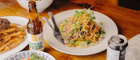 Una mesa de comedor con diversos platos, entre ellos una ensalada, papas fritas y una botella de cerveza.