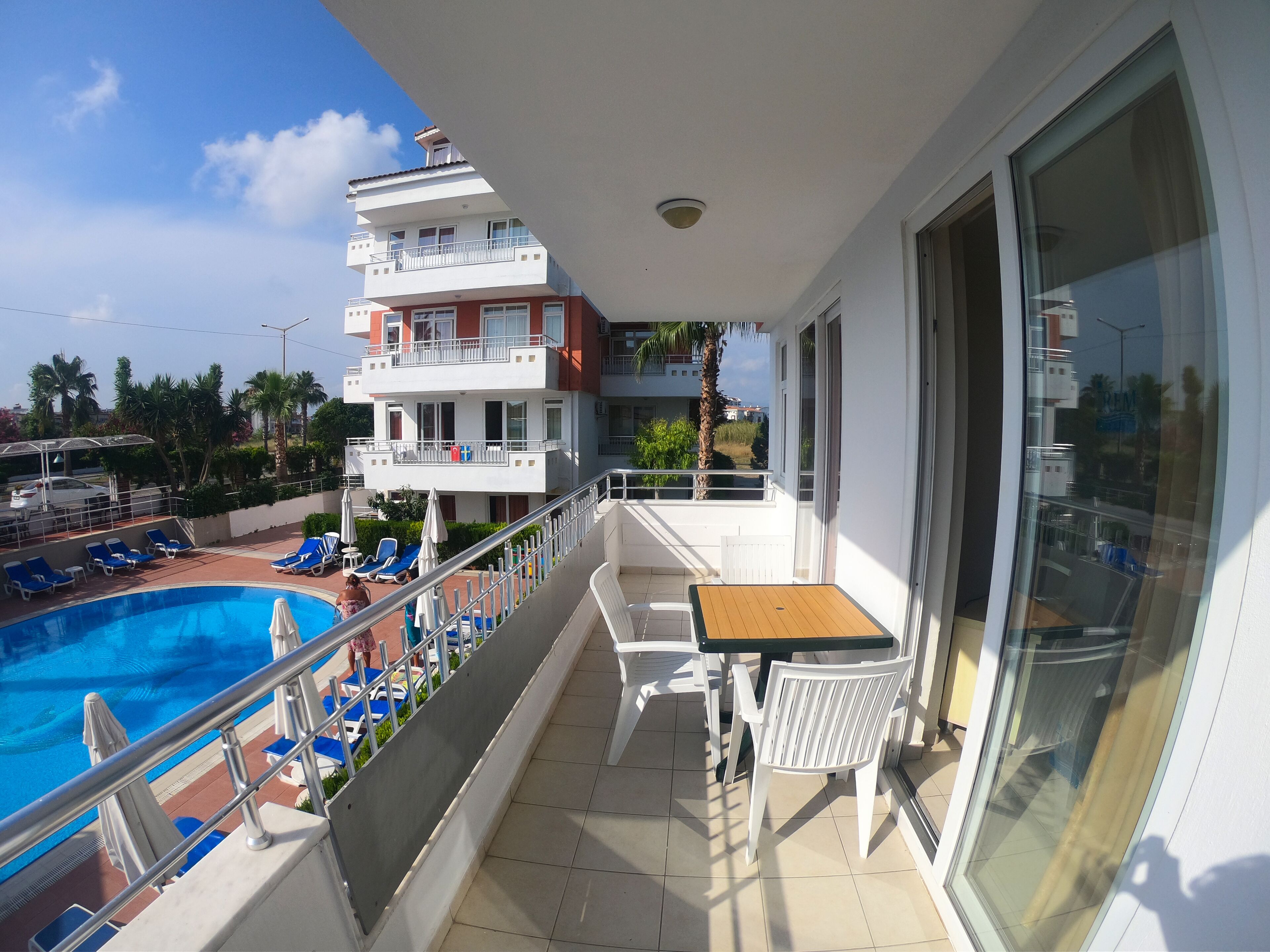 A balcony with a pool, lounge chairs, and a table.