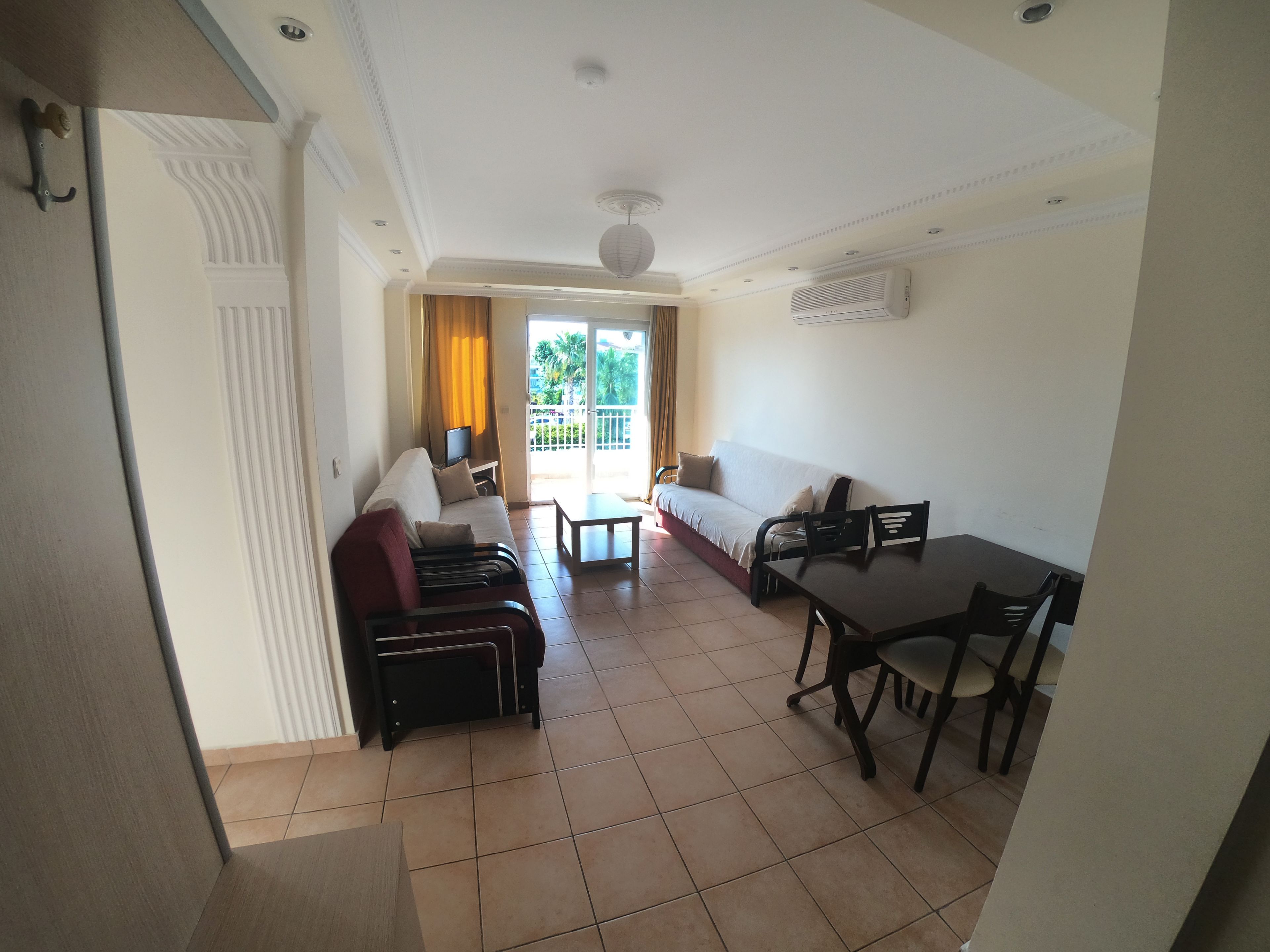 Une chambre d’hôtel avec un canapé, une table à manger, des chaises, une télévision et un balcon avec des rideaux.