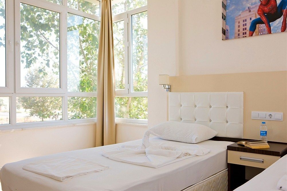 Ein Hotelzimmer mit Bett, Nachttisch, Lampe und einem Fenster mit Vorhängen.