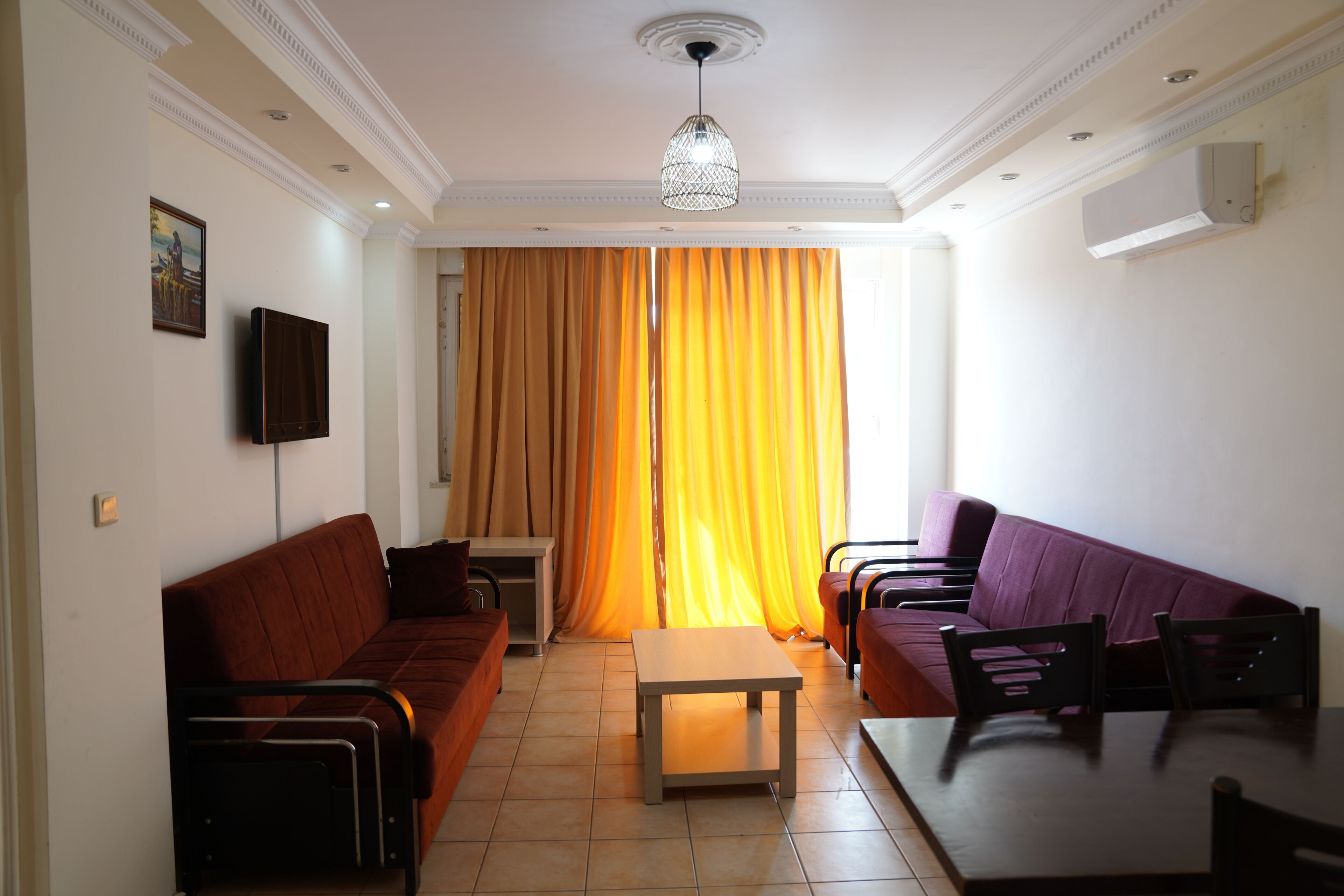 A living room with a brown sofa, a purple sofa, a wooden coffee table, and a TV mounted on the wall.