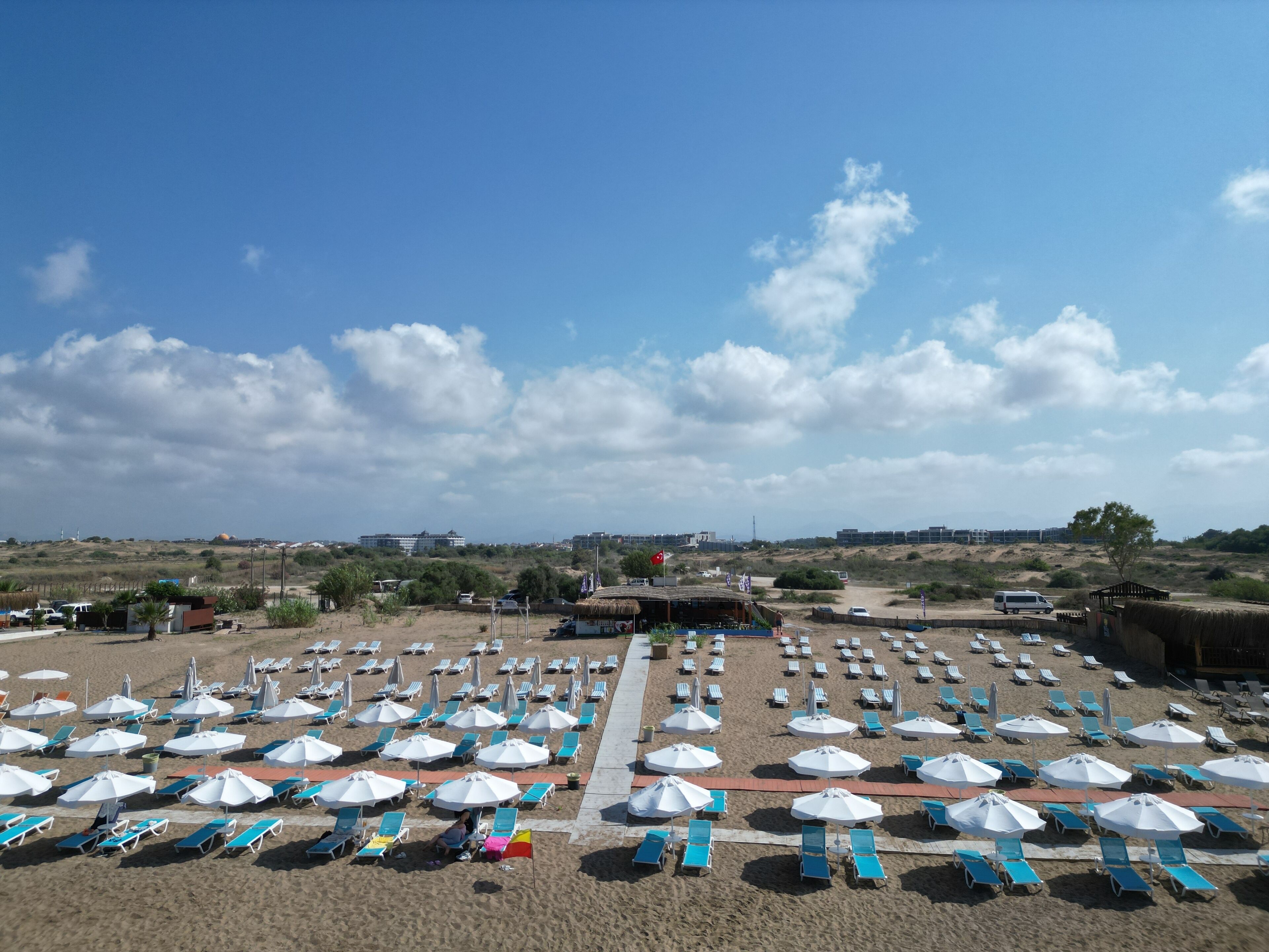 A beach with rows of sun loungers and umbrellas, a clear sky, and distant buildings.